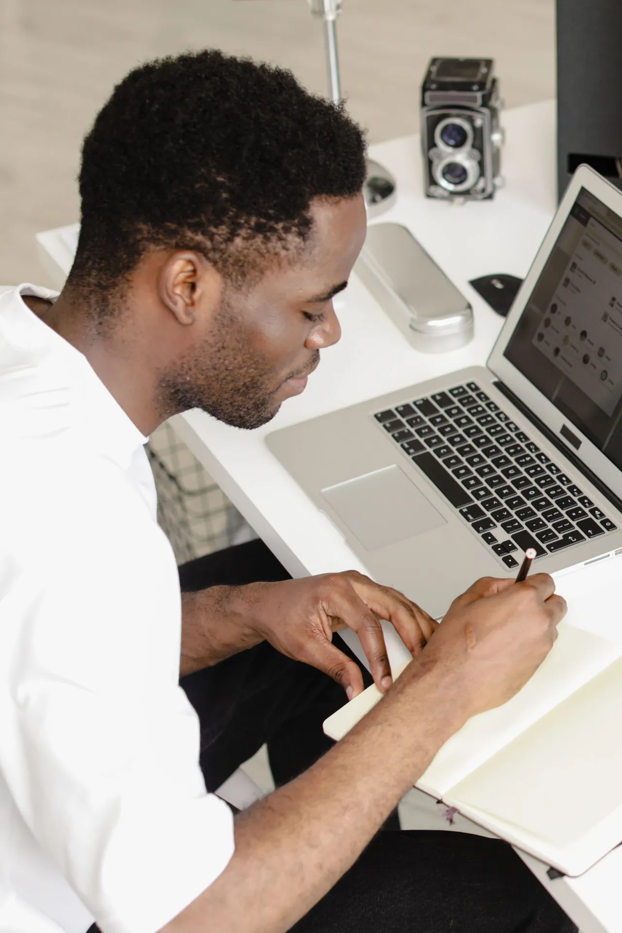 A man writing in a notebook next to an open laptop