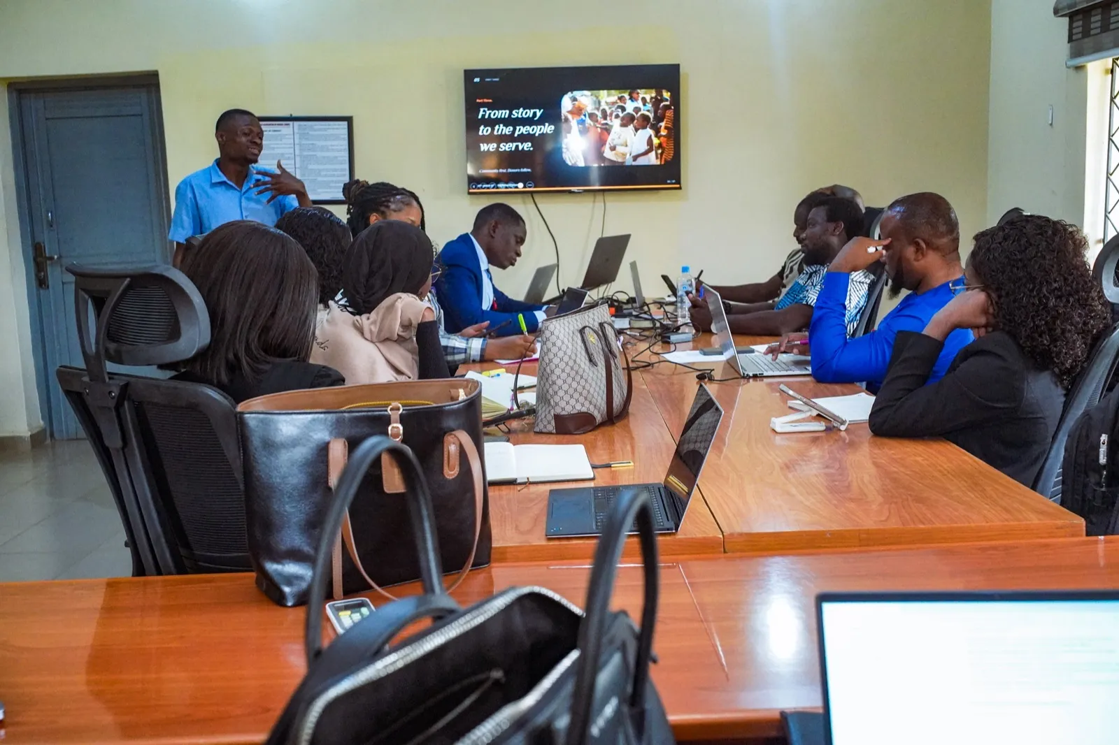 A team follows a training session around a table, facing a screen about stories.