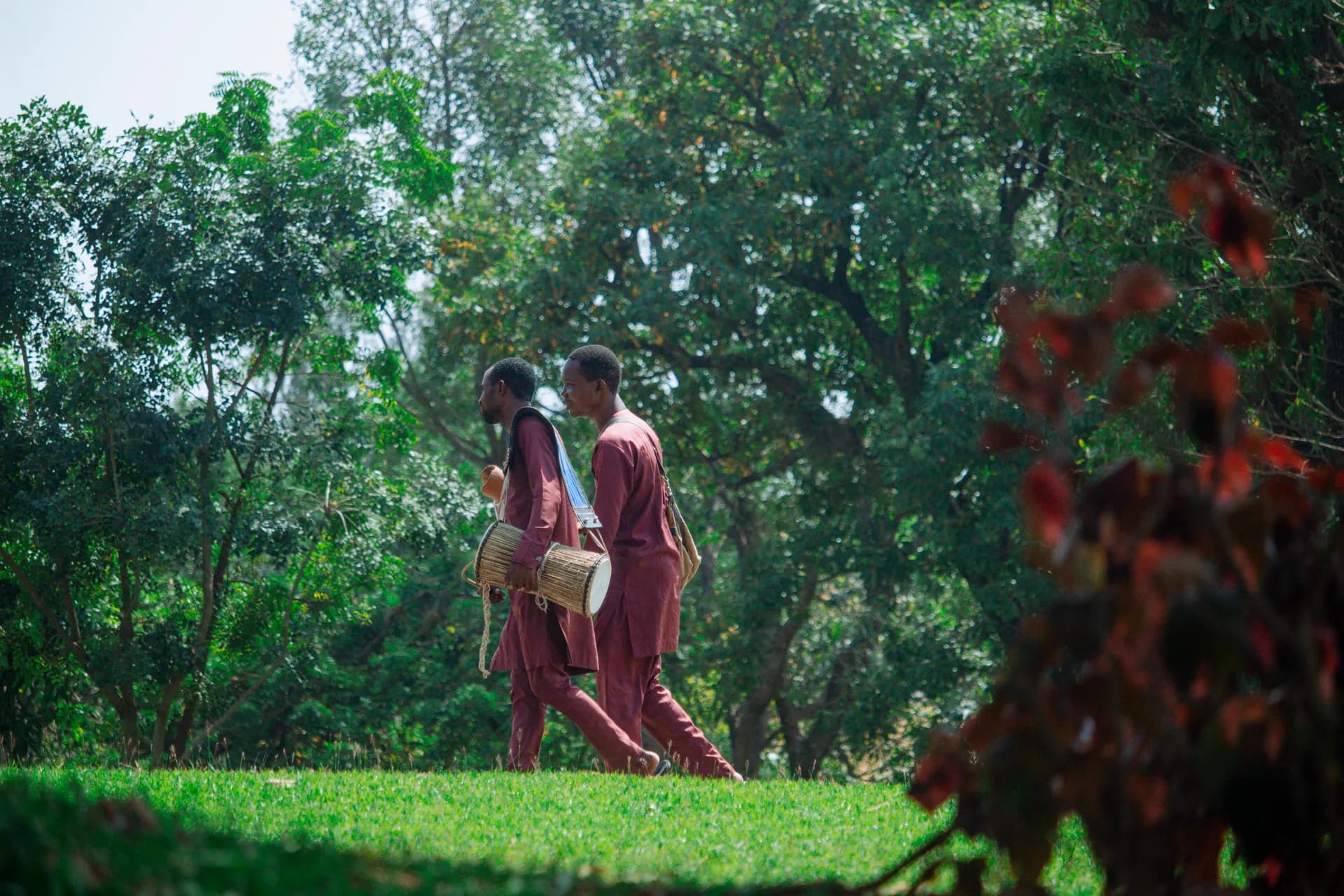 Two drummers walk together along a green path carrying their instruments.