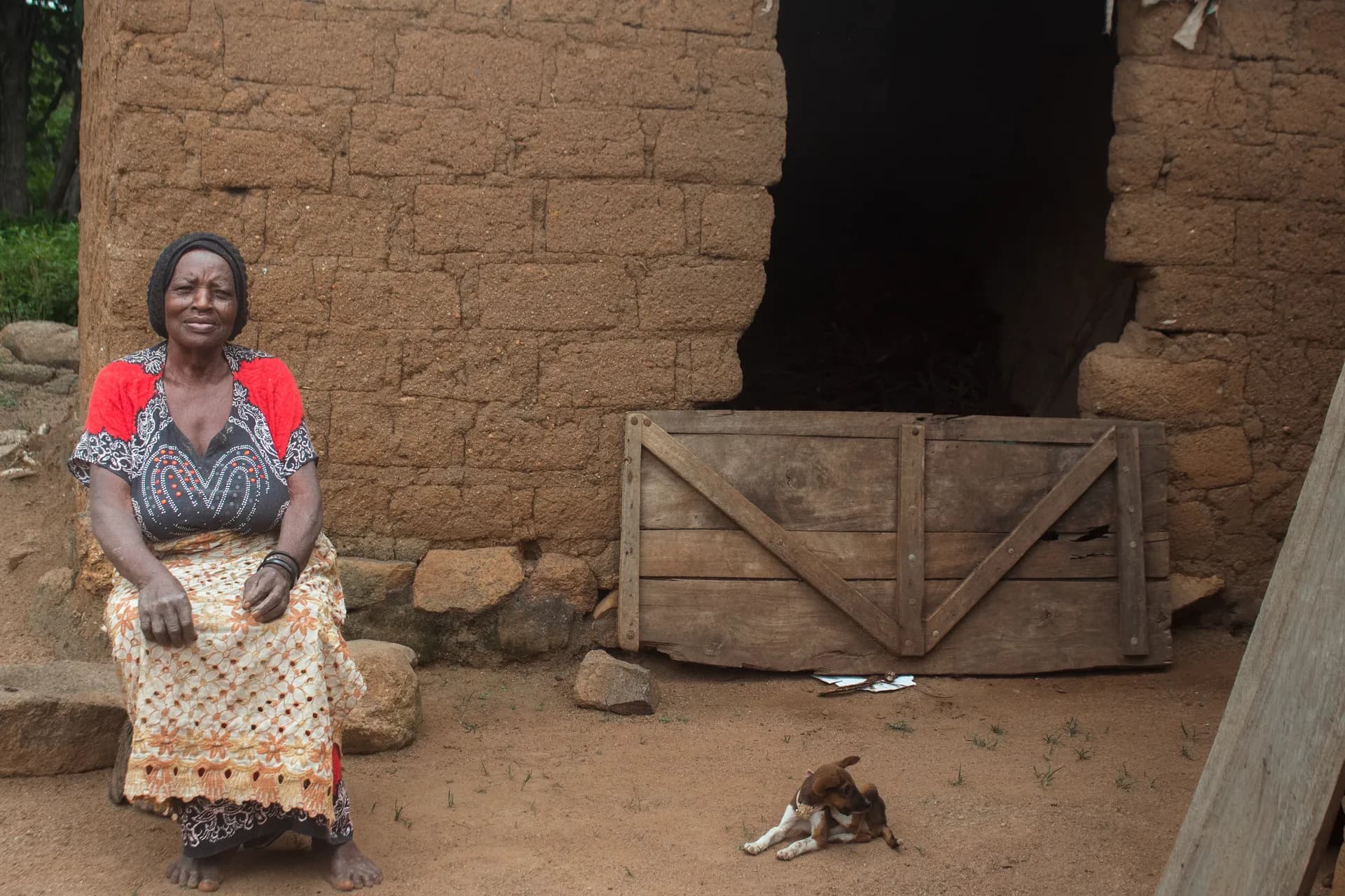 A woman seated outside a mud-brick house
